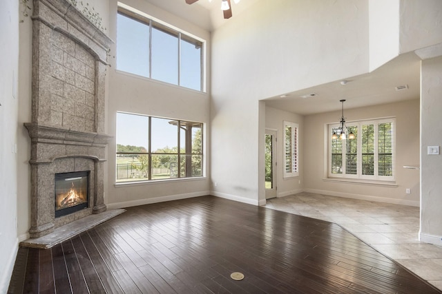 unfurnished living room with a high ceiling, ceiling fan with notable chandelier, and hardwood / wood-style flooring