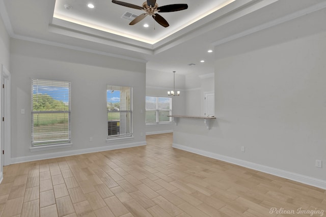 empty room featuring crown molding, light wood-type flooring, a tray ceiling, and ceiling fan with notable chandelier