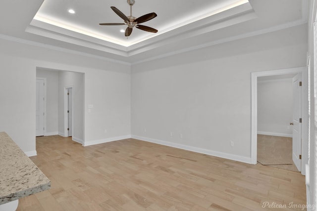 empty room with ceiling fan, a raised ceiling, and light hardwood / wood-style flooring