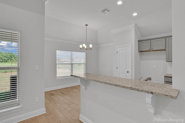 kitchen with a notable chandelier, gray cabinets, ornamental molding, light hardwood / wood-style flooring, and light stone counters