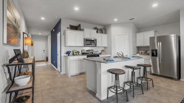 kitchen with light tile patterned floors, appliances with stainless steel finishes, a kitchen island with sink, and white cabinetry