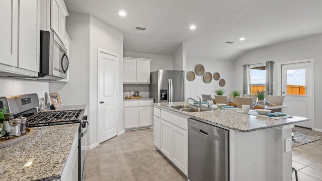 kitchen with appliances with stainless steel finishes, white cabinets, a kitchen island with sink, and light tile patterned floors