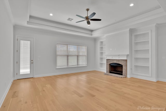 unfurnished living room featuring light wood-type flooring, a tray ceiling, a brick fireplace, and a healthy amount of sunlight