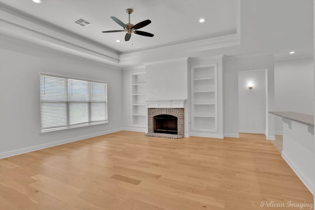 unfurnished living room featuring light wood-type flooring, a raised ceiling, built in features, ceiling fan, and a fireplace