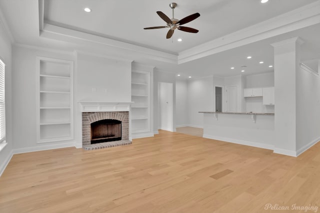 unfurnished living room featuring a raised ceiling, light hardwood / wood-style flooring, crown molding, a brick fireplace, and ceiling fan