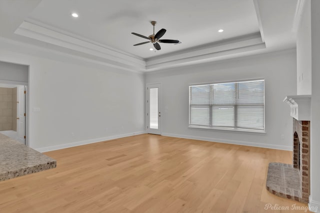 unfurnished living room with a raised ceiling, light wood-type flooring, a wealth of natural light, and a brick fireplace