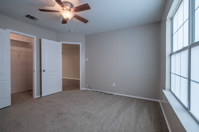 unfurnished bedroom with ceiling fan, a walk in closet, carpet floors, and multiple windows