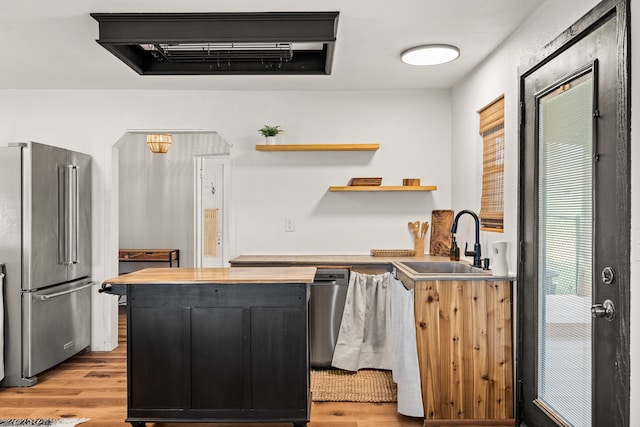 kitchen with appliances with stainless steel finishes, wooden counters, sink, and light hardwood / wood-style floors