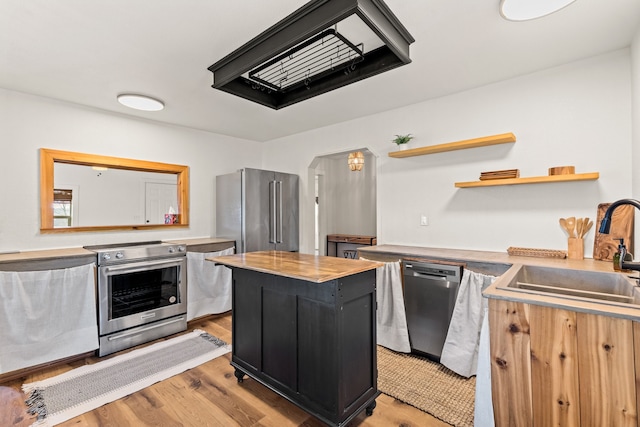 kitchen with appliances with stainless steel finishes, light hardwood / wood-style floors, a center island, sink, and butcher block counters