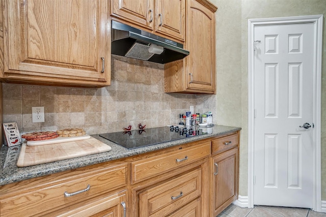 kitchen featuring light tile patterned flooring, stone counters, black electric stovetop, and backsplash