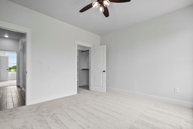 unfurnished bedroom with light carpet, a walk in closet, and ceiling fan