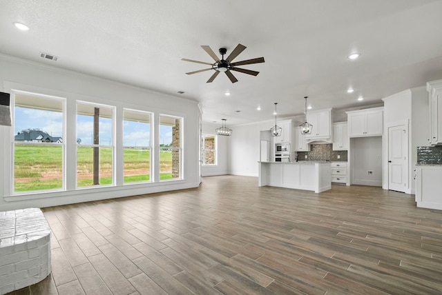 unfurnished living room featuring ornamental molding, dark wood finished floors, visible vents, and ceiling fan