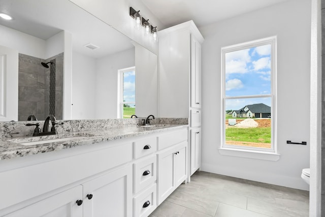 bathroom featuring vanity, toilet, a healthy amount of sunlight, and a tile shower