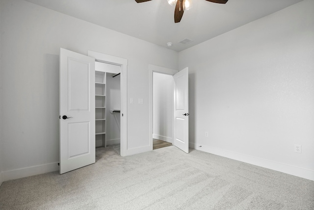 unfurnished bedroom with a spacious closet, light carpet, a closet, and ceiling fan