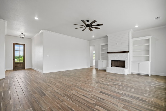 unfurnished living room with ceiling fan, a textured ceiling, light wood-type flooring, a fireplace, and crown molding