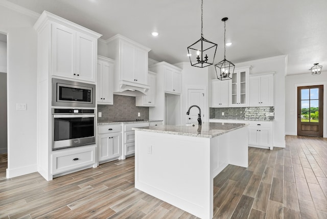 kitchen featuring light hardwood / wood-style flooring, an island with sink, white cabinetry, appliances with stainless steel finishes, and light stone counters