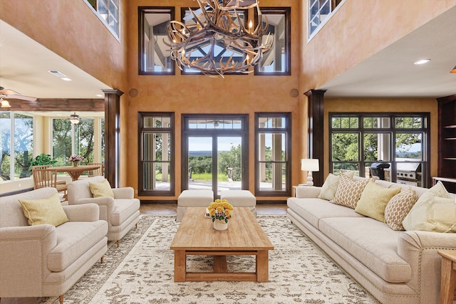 living room with ceiling fan with notable chandelier, a towering ceiling, light hardwood / wood-style floors, and ornate columns