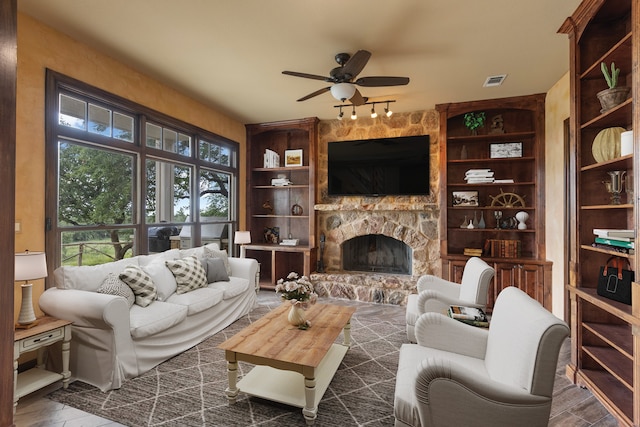 living room featuring ceiling fan, dark hardwood / wood-style flooring, built in features, and a stone fireplace