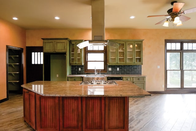 kitchen with light wood-type flooring, plenty of natural light, light stone countertops, and decorative backsplash