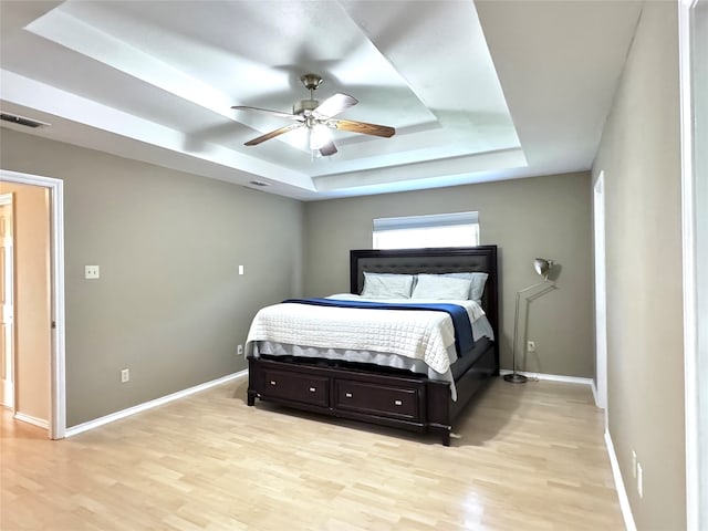 bedroom with light hardwood / wood-style flooring, ceiling fan, and a raised ceiling