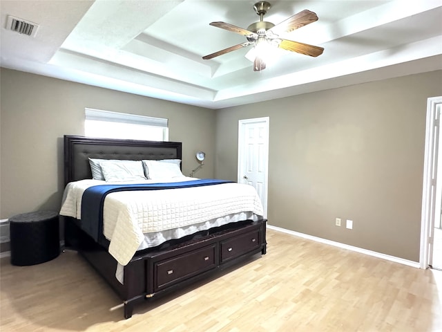 bedroom with ceiling fan, light hardwood / wood-style floors, and a tray ceiling