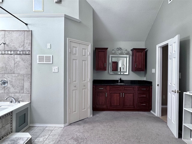 bathroom featuring vaulted ceiling, a bathing tub, a textured ceiling, and vanity