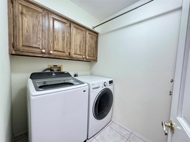 clothes washing area featuring washing machine and dryer, light tile patterned floors, and cabinets