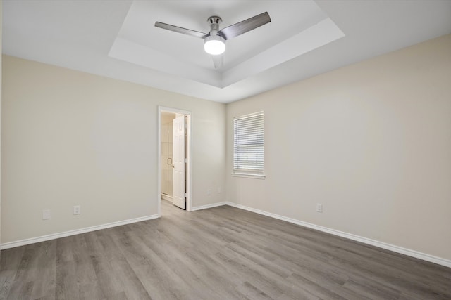 empty room with ceiling fan, wood-type flooring, and a tray ceiling