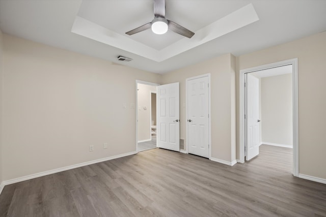 unfurnished bedroom with ceiling fan, a tray ceiling, and hardwood / wood-style floors