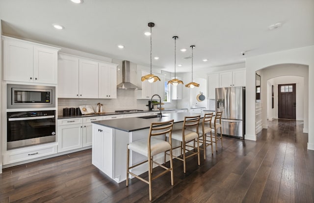 kitchen featuring stainless steel appliances, wall chimney exhaust hood, decorative light fixtures, white cabinets, and dark hardwood / wood-style flooring