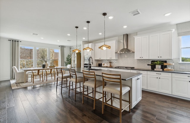 kitchen with dark hardwood / wood-style flooring, wall chimney range hood, a center island with sink, and white cabinets