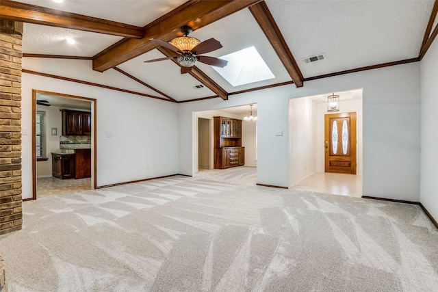 empty room featuring vaulted ceiling with skylight, visible vents, baseboards, light colored carpet, and ornamental molding