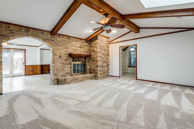 unfurnished living room featuring ceiling fan, brick wall, a brick fireplace, vaulted ceiling with skylight, and carpet floors