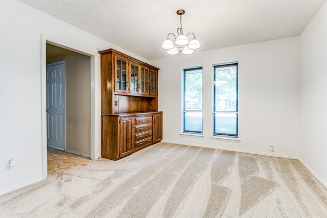 unfurnished dining area with a textured ceiling, an inviting chandelier, and light carpet