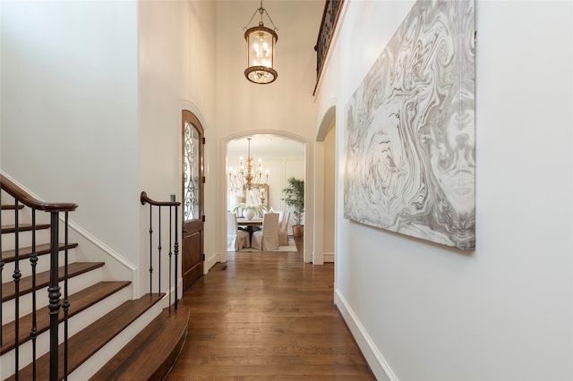 hallway with an inviting chandelier, hardwood / wood-style floors, and a high ceiling