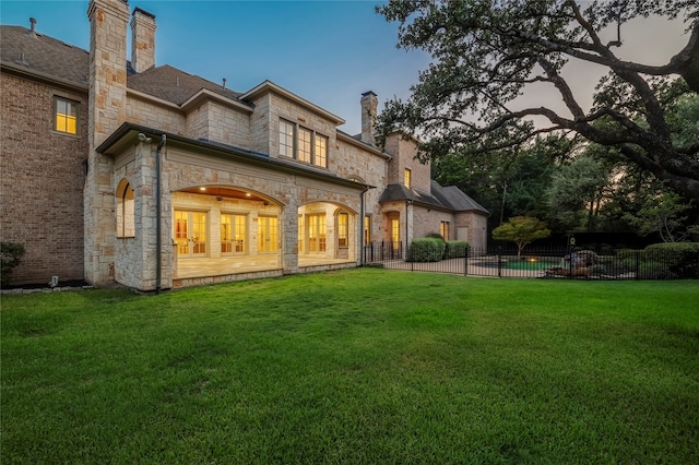 back house at dusk featuring a lawn