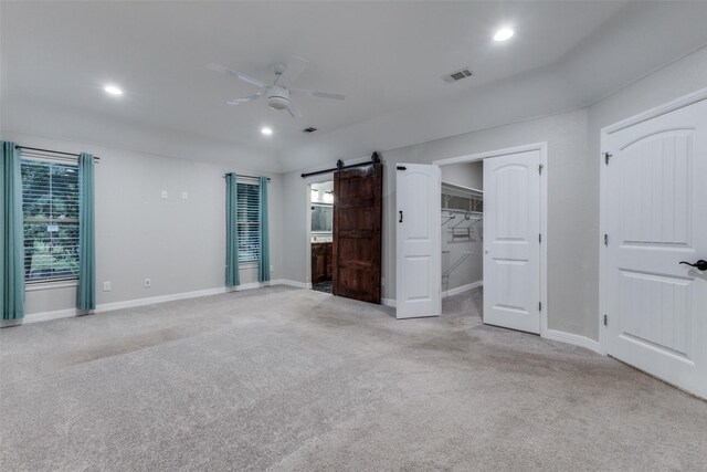 unfurnished bedroom with light colored carpet, a barn door, multiple windows, and ceiling fan