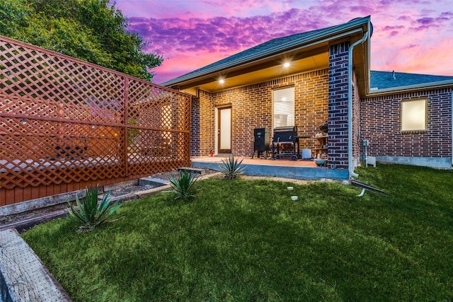 back house at dusk featuring a patio and a lawn