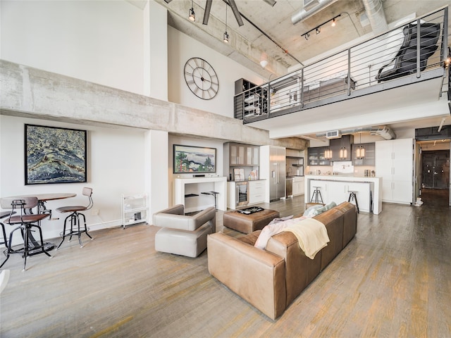 living room with a towering ceiling, rail lighting, and hardwood / wood-style floors