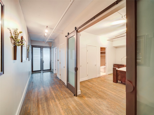 hallway featuring a barn door, baseboards, wood finished floors, and french doors