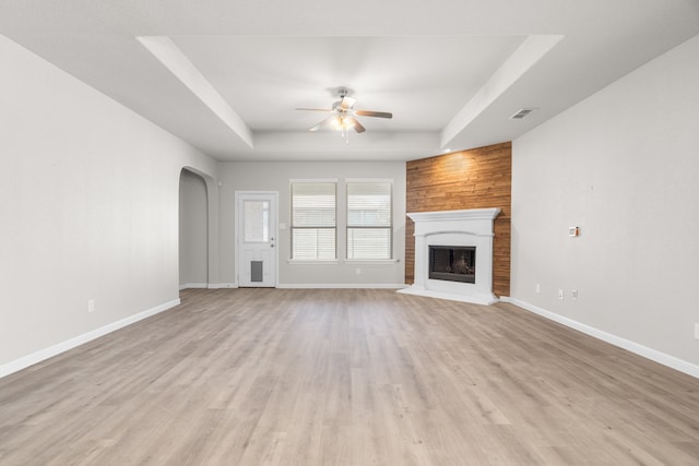 unfurnished living room with light hardwood / wood-style floors, wood walls, a tray ceiling, and ceiling fan