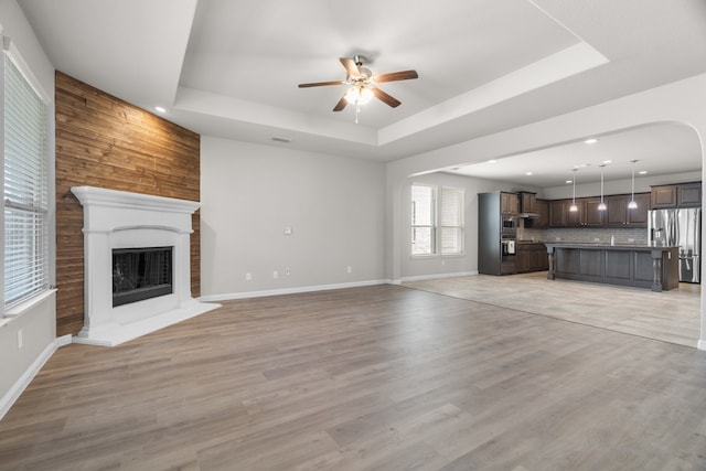 unfurnished living room featuring light hardwood / wood-style floors, wood walls, a tray ceiling, and ceiling fan