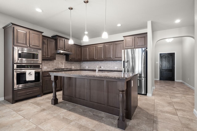 kitchen with stone counters, dark brown cabinets, an island with sink, and stainless steel appliances