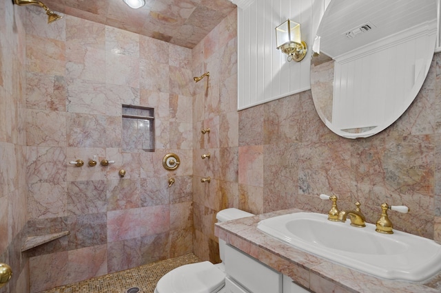 bathroom with a tile shower, tile walls, vanity, and toilet