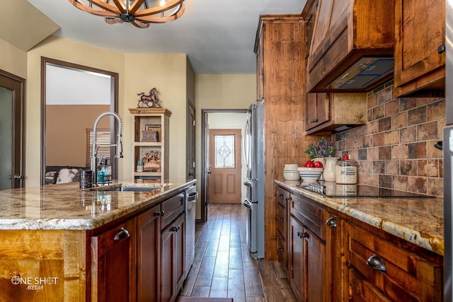 kitchen with a kitchen island with sink, sink, light stone counters, black electric stovetop, and decorative backsplash