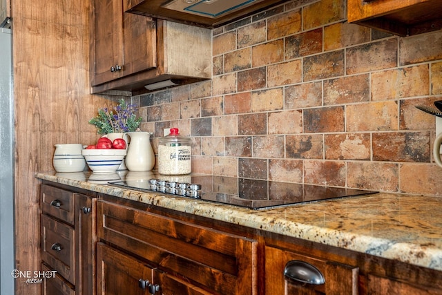 kitchen featuring decorative backsplash, dark brown cabinets, black electric cooktop, and light stone counters