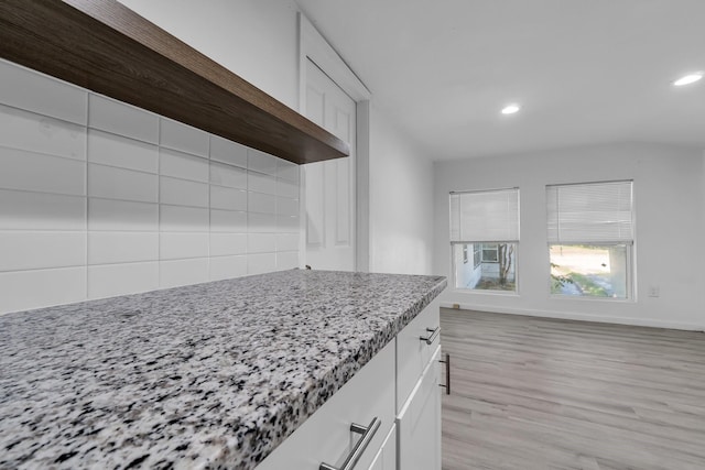 kitchen with white cabinetry, light stone countertops, and light wood-type flooring