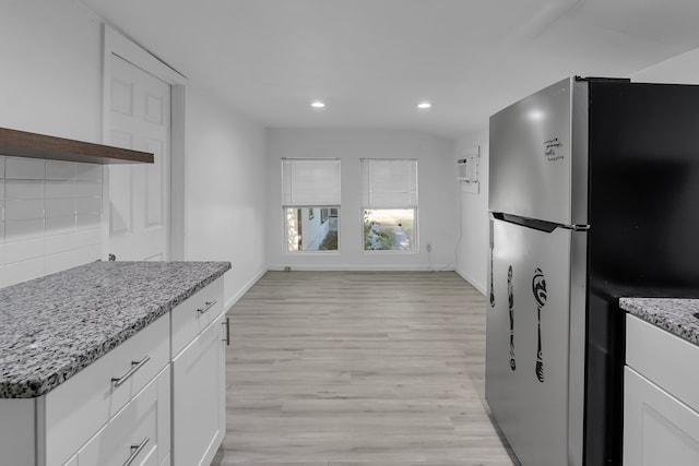 kitchen featuring backsplash, white cabinets, stainless steel fridge, light stone countertops, and light wood-type flooring