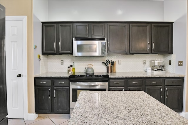 kitchen with backsplash, appliances with stainless steel finishes, light stone counters, and light tile patterned floors