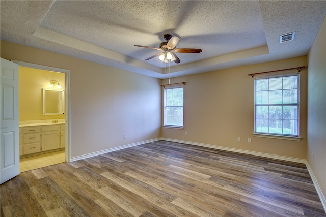 unfurnished bedroom featuring multiple windows, light wood-type flooring, and a raised ceiling